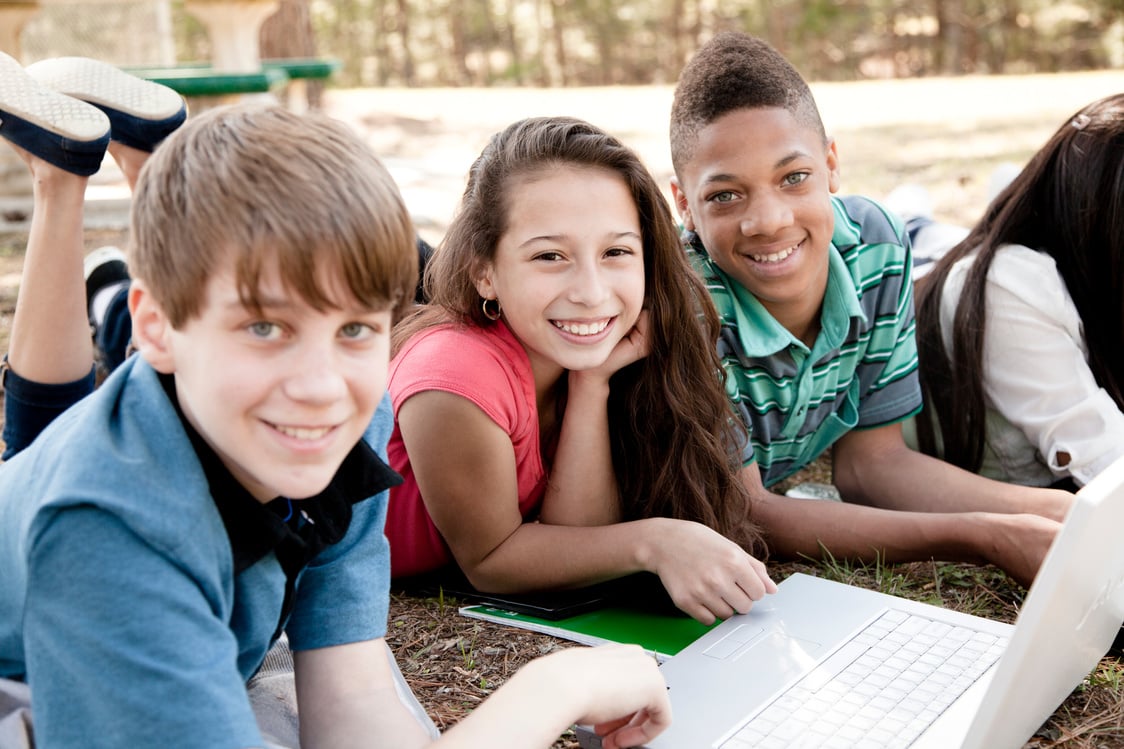 Technology:   Junior high students using laptop to study outside.